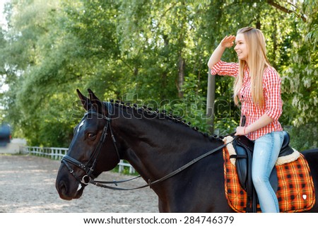 Where are you. Young smiling girl holding her hand near the forehead while sitting in the saddle.