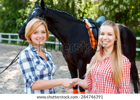 Amicable relationships. Smiling girls having optimistic mood and shaking hands with dark horse standing in the background.