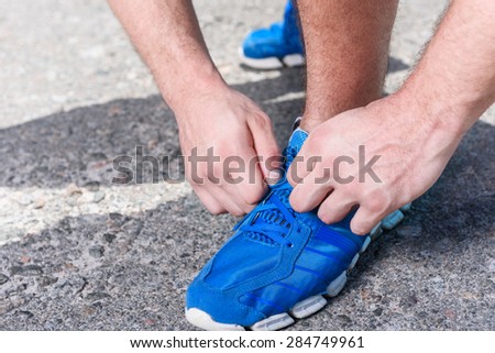 Close up photo of a muscled sportsman tying shoelaces on his blue running sneakers , wearing black white sportswear during training in the park