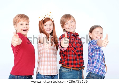 Life is great. Joyful children thumbing up and smiling while standing isolated on white background.
