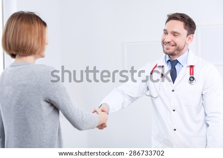 Good bye. Smiling professional doctor shaking hands with the patient and looking at her while leaving.