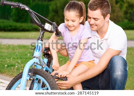 Portrait of a caring father repairing something in the blue bicycle standing upside down and his small daughter trying helping him happily