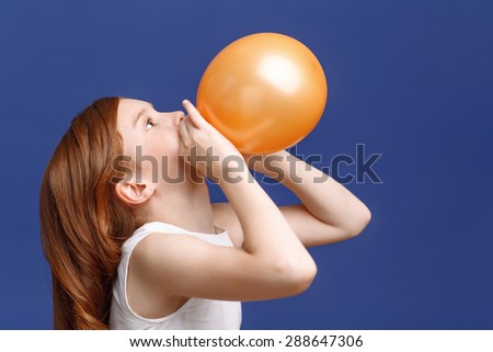 Lets have fun. Close up on pretty young red-haired girl inflating balloon while standing half-turned.