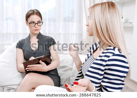 Portrait of a psychologist sitting on a couch listening to her client telling about her problems during therapy session, selective focus