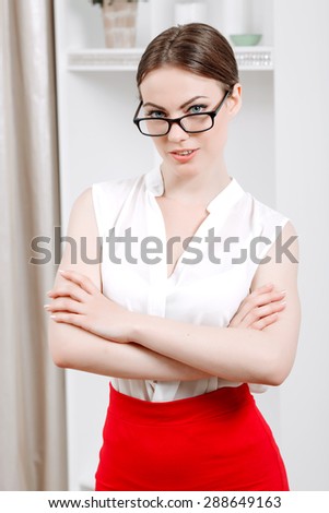 Portrait of a beautiful woman wearing white blouse and red skirt and glasses, standing and looking seductively in a light room