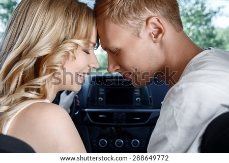 Sweet couple. Portrait of a young beautiful blond woman with curvy hair and her handsome boyfriend sitting in a car hording their heads near and smiling