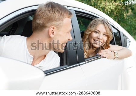 Happy journey. Portrait of a handsome young man looking out of the window of the car on his beautiful blond girlfriend with curvy hair sitting in the back seat smiling