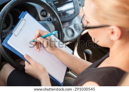 Working on way. Top view of young busy woman sitting insid car and signing papers.