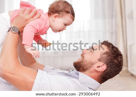 Happy moment. Upbeat young father keeping his hands up and holding his kid while rejoicing in warm atmosphere.