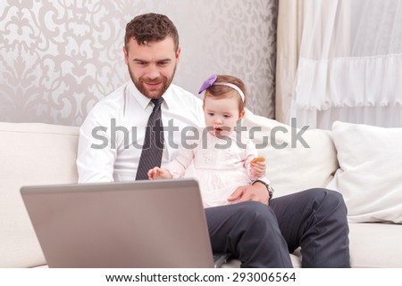 Checking e-mail. Nice positive dad holding baby and working with laptop while sitting on the sofa