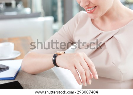 Portrait of a beautiful businesswoman wearing beige dress sitting at the table looking at her watch waiting for her partners, in a restaurant during business lunch