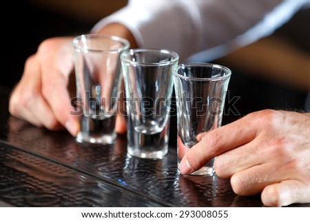 Close up photo of hands of a bartender putting shot glasses on a wooden counter