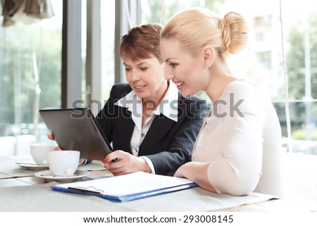 Portrait of a beautiful businesswoman wearing  formal suit sitting at the table holding a tablet and discussing business matters with her colleague looking at it, in a restaurant during business lunch