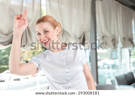 Waist up portrait of a beautiful businesswoman wearing a beige blouse standing holding her hand up calling a waiter or her colleague, in a restaurant during business lunch, selective focus