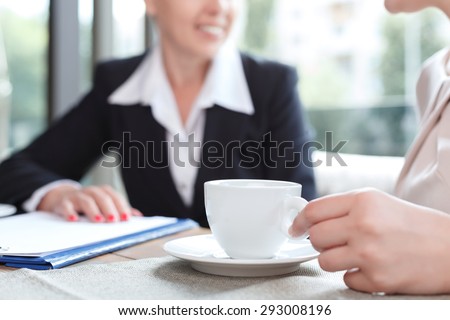 Close up photo of a hand of a woman holding a cup of coffee and her business partner, in a restaurant during business lunch, selective focus