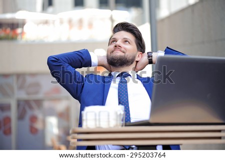 Time to relax. Nice handsome bearded businessman keeping his hands behind  neck and looking up while sitting at the table.