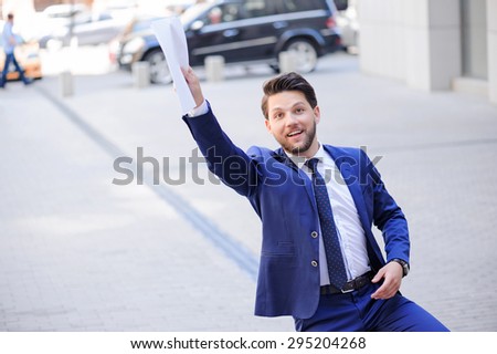 Hey. Nice bearded businessman keeping his hand up and holding papers while expressing positivity.