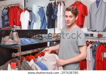 What to choose. Portrait of young-looking handsome man standing in boutique and choosing shirt for himself.