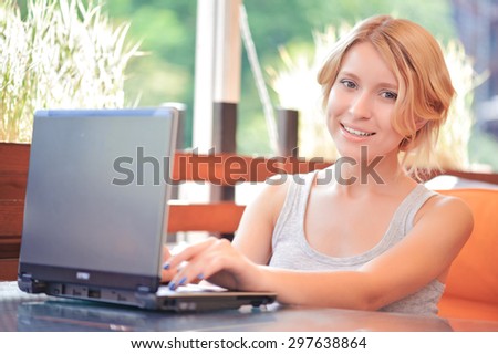 Checking e-mails. Young  pretty smiling blond-haired girl in cafe and using her new laptop.