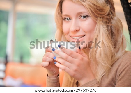 Coffee time. Portrait of young pretty blond-haired woman holding cup with coffee in cafe