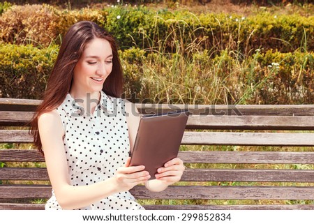 It is time to surf worldwide network. Waist up of pleasant smiling girl holding laptop and surfing  the Internet while sitting on bench
