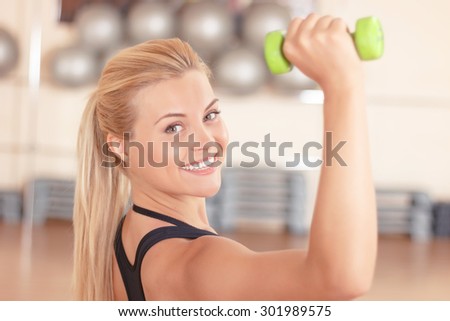 Keeping fit. Beautiful smiling woman doing fitness exercises by using little dumbbells in gym