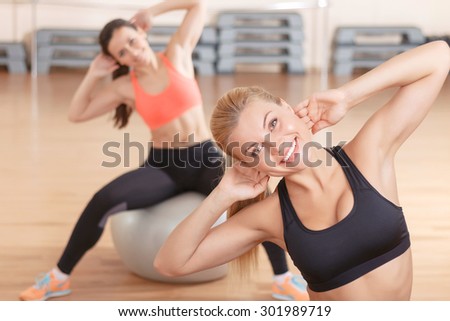 Stretch and relax. Two young pretty woman sitting on fitness balls and doing stretching exercises in gym.
