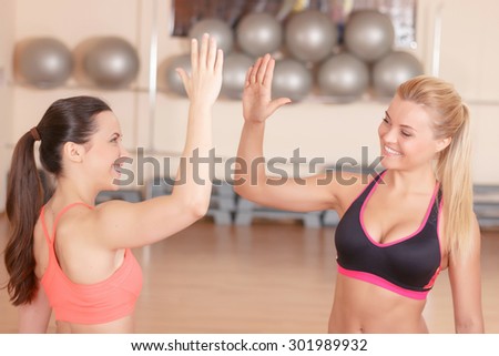 Nice meeting. Two beautiful sportive girlfriends giving high five in gym .