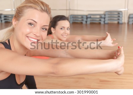 Leaning to purpose. Pretty blond-haired woman with her friend doing stretching exercises by leaning forward.