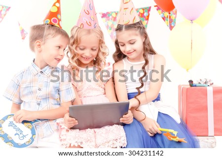 Different emotions. Group of little cheerful kids sitting at table during birthday party.