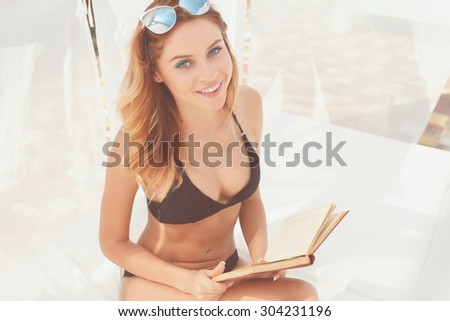Love story. Top view of pretty smiling young red-haired woman in bikini holding book at pool
