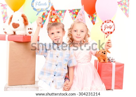 Birthday signs. Little nice boy and girl sitting on background of lots presents holding tags with birthday related signs.