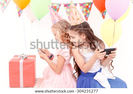 What is she doing. Little chic girl sitting back to another with mobile phones during birthday party and looking at her device.