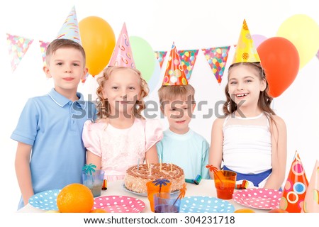 Happy childhood. Group of funny little children standing at adorned table with birthday cake on it during party.