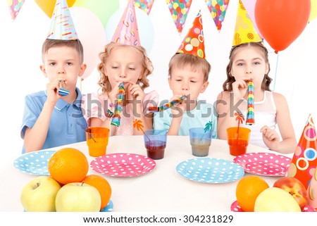 Birthday signal. Group of little cute children sitting at table and blowing party horn