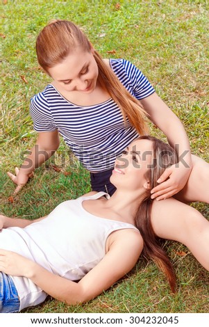 Lovely glance. Young smiling women lying on knees of another and they are looking at each other in park