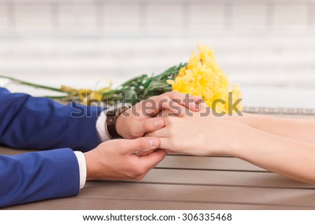 Holding fast. Man holding hands of his lovely girlfriend on background of flowers.