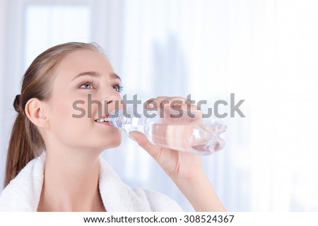 Open your mind. Beautiful happy young lady holding bottle and drinking water while keeping glance up