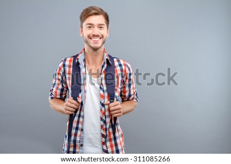 Feeling over the moon. Pleasant young student holding bag traps and expressing joy while standing isolated on grey background
