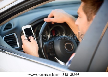 Be modern. Nice upbeat young man holding mobile phone and holding steering wheel while driving his car
