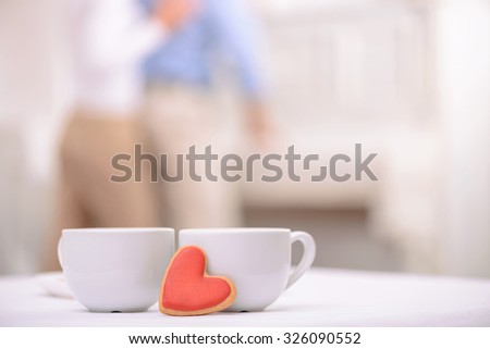 Warm your heart. Two cups of tea standing on the table with adult couple embracing on the background