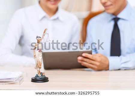 Good professionals. Close up of little statue of justice standing on the table with two professional lawyers working on the background