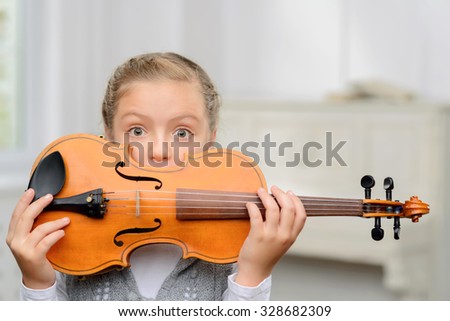 Happy childhood. Pleasant positive little girl holding violin in front of her face and hiding behind it while having music lesson