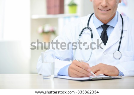 Best professional. Pleasant cheerful delighted doctor making notes and sitting at the table while being busy at work