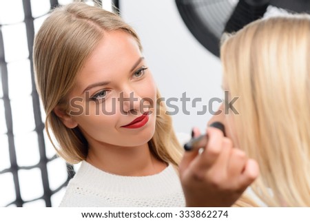Decent attitude. Female makeup artist looks trusting when smiles during her accurate work.