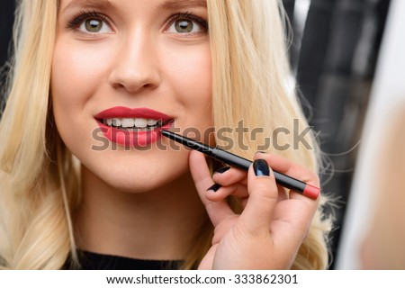 Red lipstick spreading. Female nice-looking model waits while red lipstick is being applied by makeup artist.