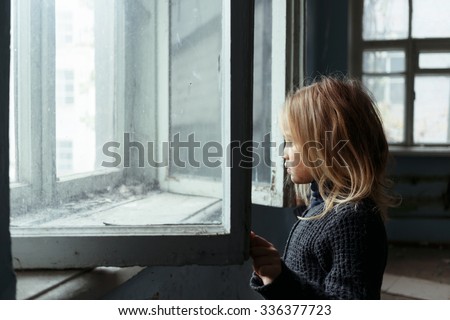 Hopeless glance. Poor unhappy cheerless girl looking outside and standing near window while feeling hopeless