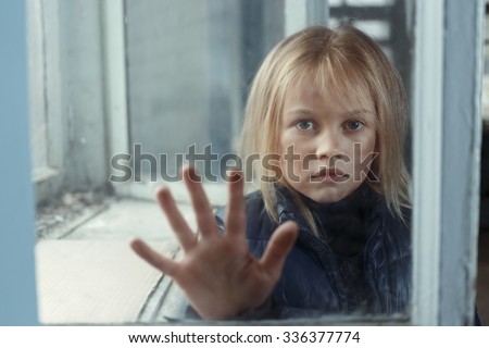 Help me. Little poor miserable girl  standing near window and begging for help while  holding her hand on glass