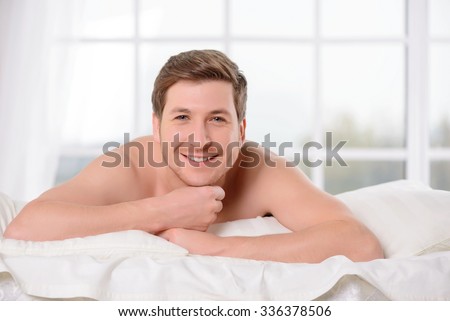Good morning. Good-looking young man smiles genuinely after waking up in comfortable bed.