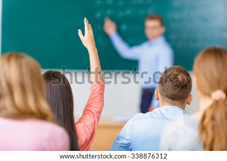Desire to answer. Female young student in a group raises her arm in order to answer the question.